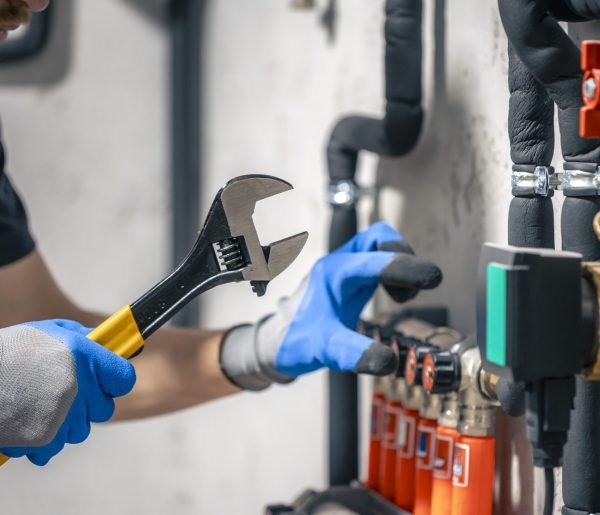 A man installs a heating system in a house and checks the pipes with a wrench. Adjusting heating valves in a residential building. A plumbing and heating technician works.